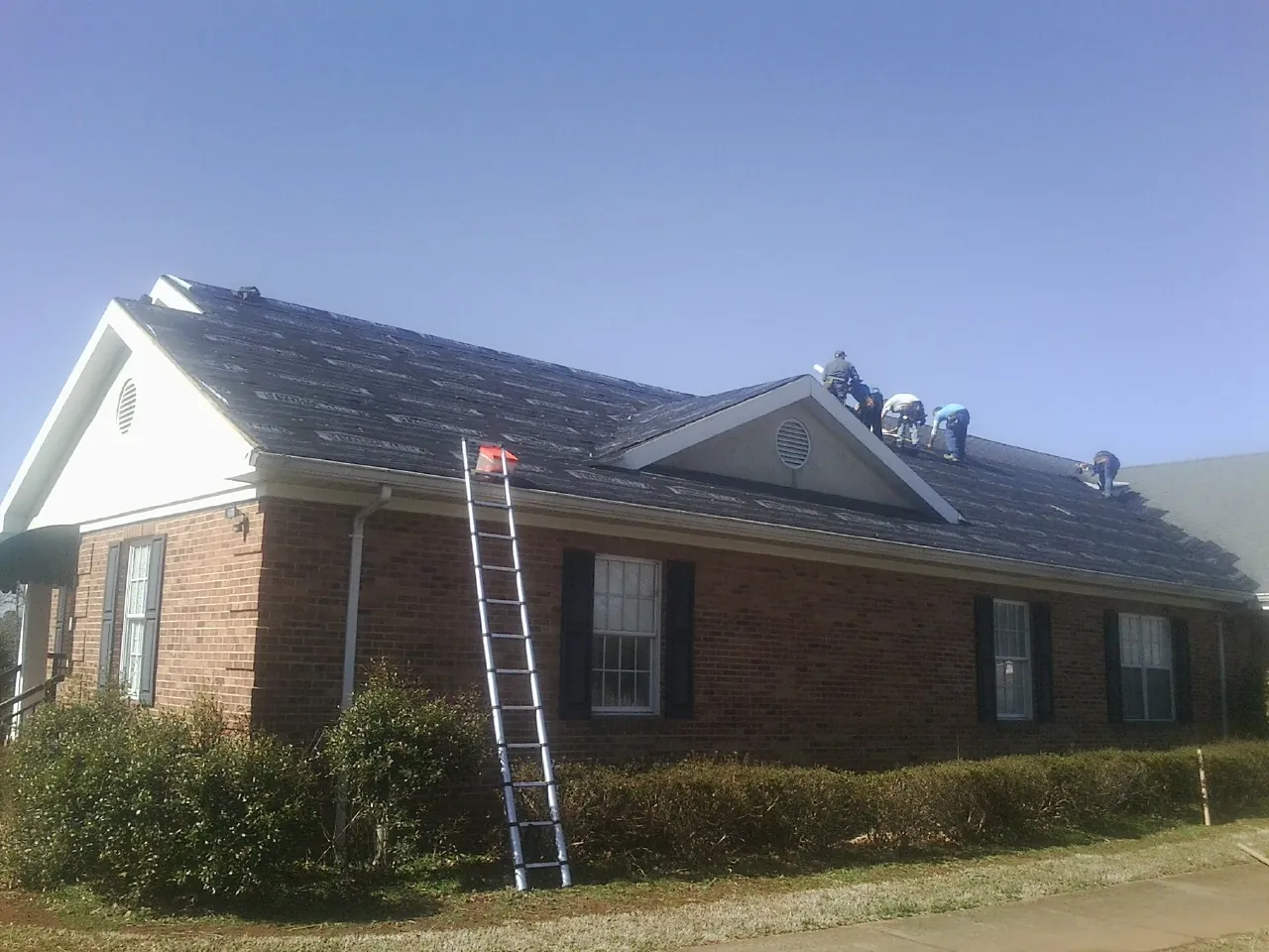 Crew tearing shingles off a brick ranch roof with a ladder set — Emergency Roof Repair work by our crew in Layton