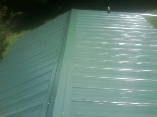 New green metal panels meeting at the ridge of a roof — Flat Roof Repair work by our crew in Layton