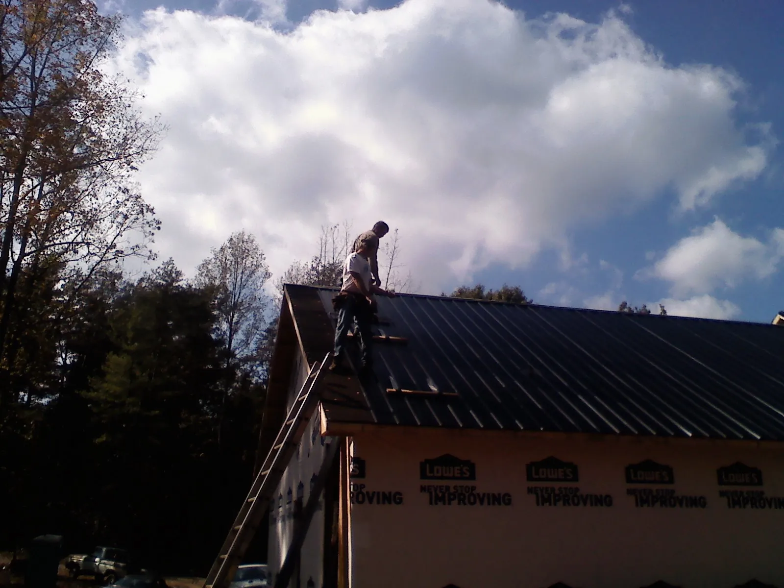 Roofer fastening dark metal panels high against a cloudy sky, from a Roof Inspection job in Layton